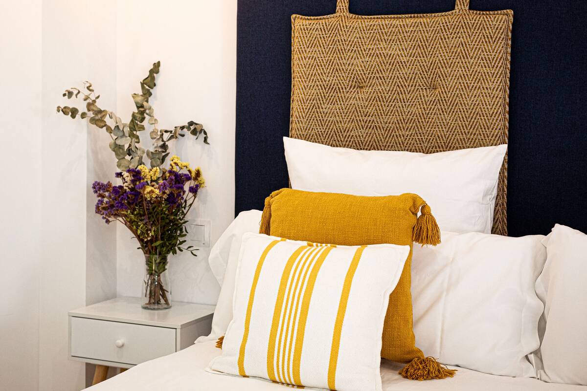 A neatly arranged bedroom with a bed, pillows, a bedside table, and a vase with flowers.