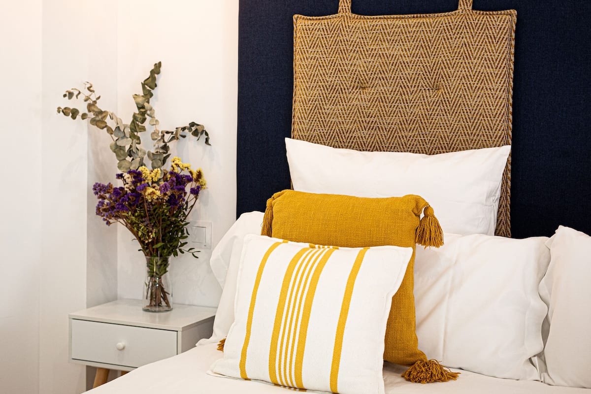 A neatly arranged bedroom with a bed, pillows, a bedside table, and a vase with flowers.
