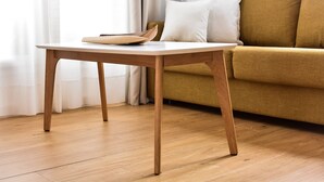 A wooden table with a white surface and a brown object on it, positioned in front of a mustard-colored sofa with white cushions. - 7escalones Apartamentos Boutique (Rota)