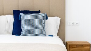 A bed with a beige headboard, white and blue striped pillows, and a beige blanket. - 7escalones Apartamentos Boutique (Rota)