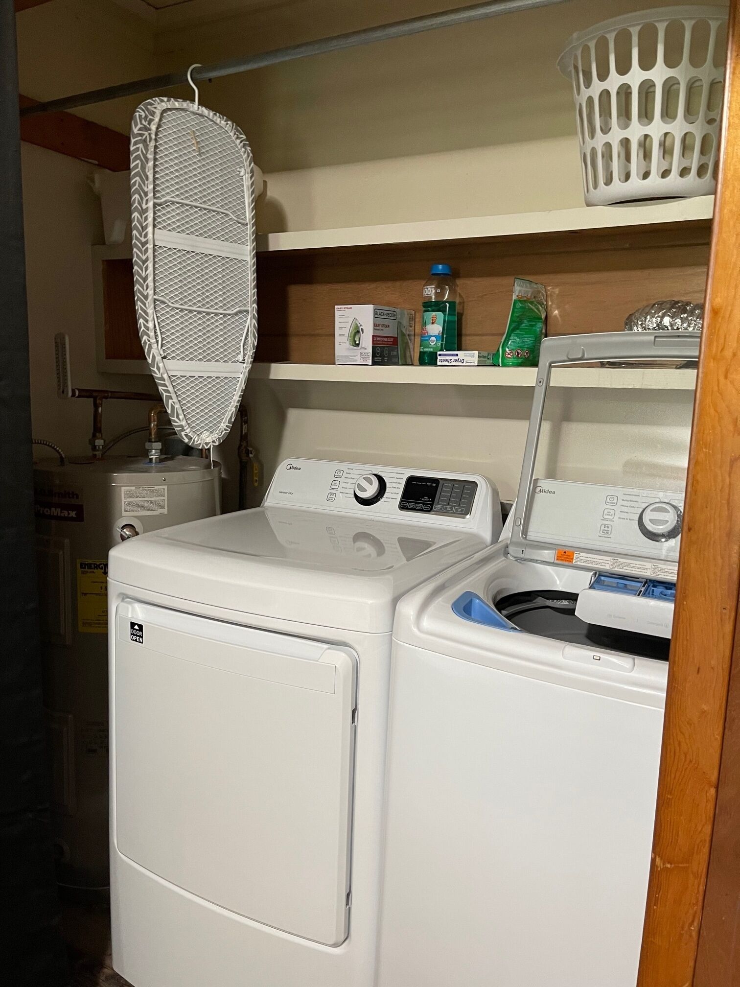 A laundry area with two washing machines, a drying rack, and shelves with cleaning supplies.