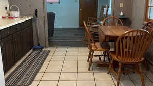 Een eetgedeelte met een houten tafel en stoelen, een keuken met kastjes en een magnetron, en een trap die naar een ander niveau leidt.