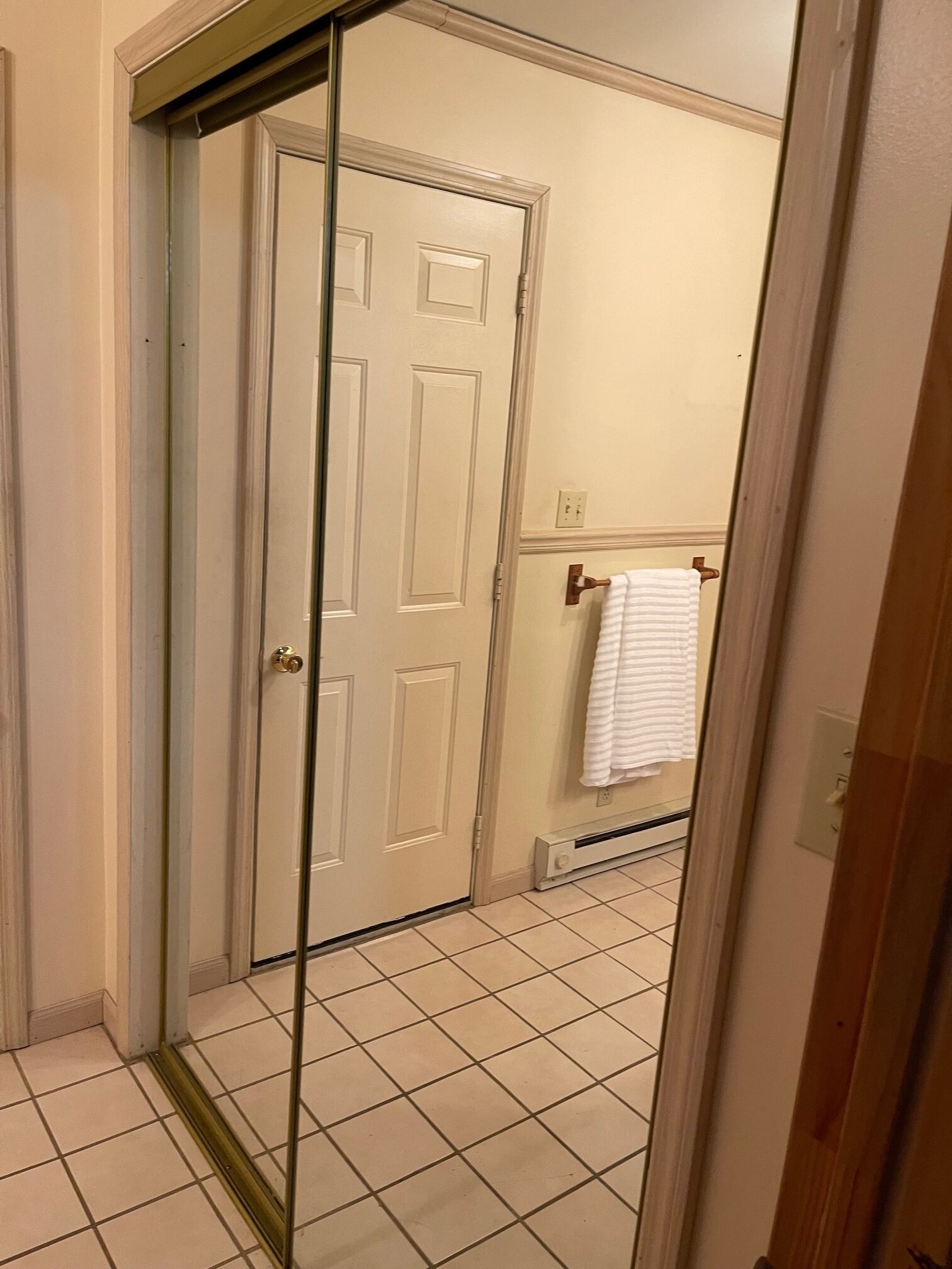 Un couloir avec une porte blanche, un sol carrelé et une serviette suspendue à un porte-serviettes.