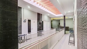 Passadís modern d'hotel amb barana blanca, escala amb accents rosats i vista a una habitació amb paret de textura fosca.