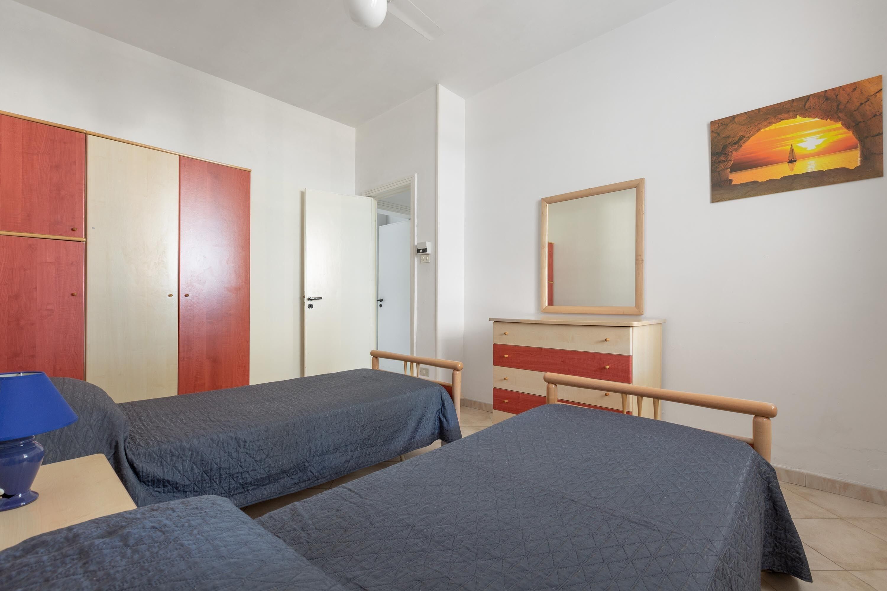 Quarto com duas camas, penteadeira, espelho e pintura de um pôr do sol.