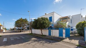 Una calle residencial tranquila con una casa blanca, un portón azul y un paso de peatones.