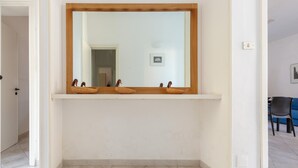 Un pasillo con un espejo grande en la pared, una puerta a la izquierda y una silla al fondo.