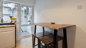 Una cocina con una mesa de madera y taburetes, un lavavajillas y una ventana con vistas a la calle.