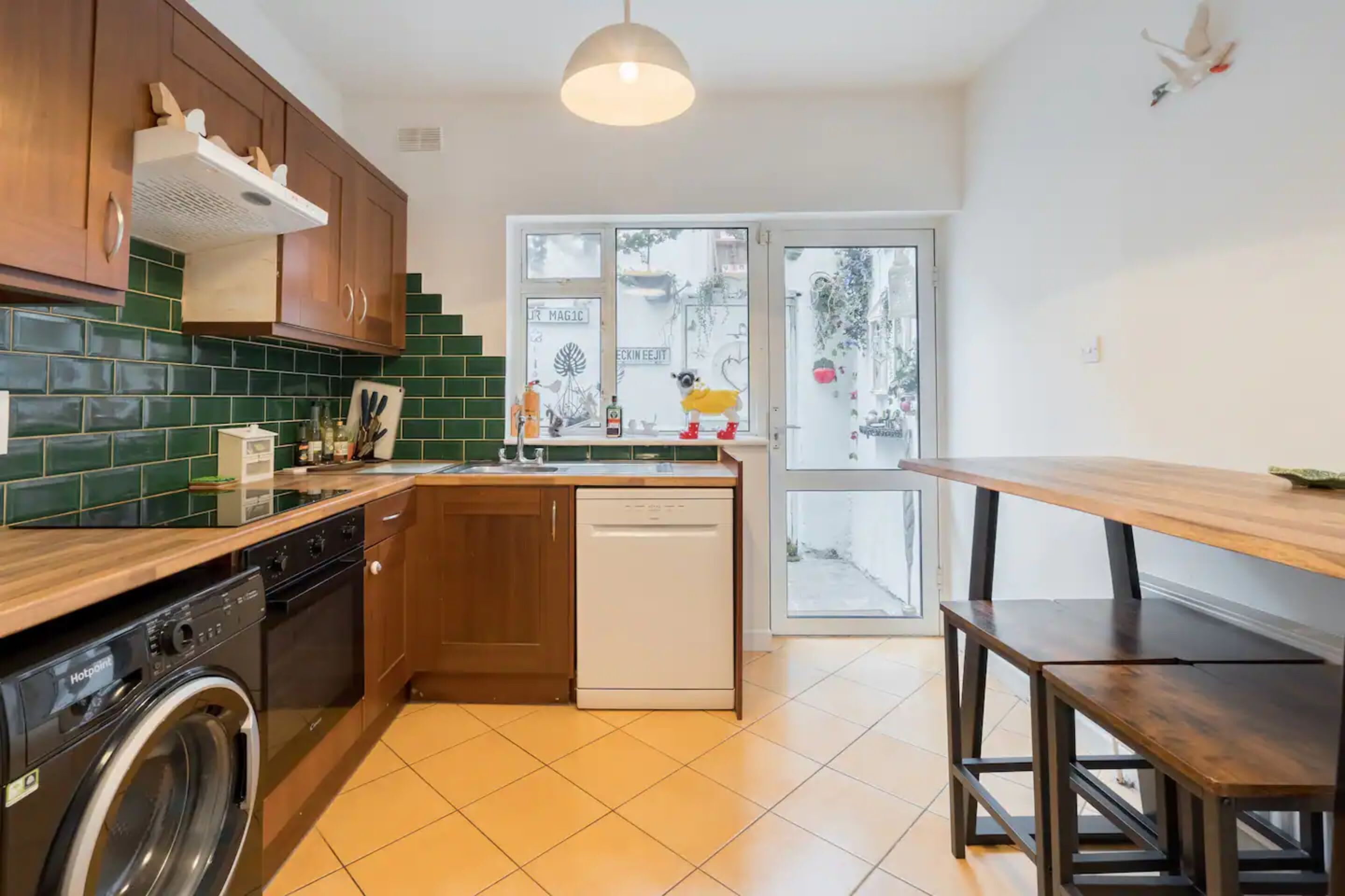 A kitchen with wooden cabinets, a dishwasher, a washing machine, a wooden dining table, and a large window with a view of the outside.