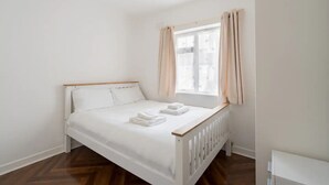 Una cama bien hecha con sábanas y toallas blancas, un cabecero de madera y una ventana con cortinas.