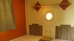 Una habitación con dos camas, una mesita pequeña y una lámpara fijada a la pared.