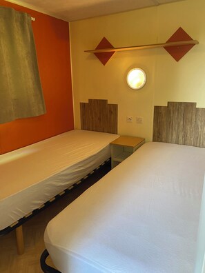 Ein Zimmer mit zwei Betten, einem kleinen Tisch und einer Wandleuchte.