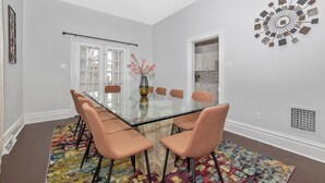 A dining area with a glass table, cushioned chairs, a colorful rug, and a decorative wall piece.