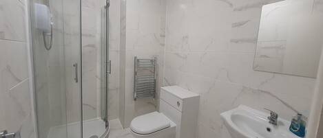 Une salle de bain avec une douche à parois de verre, des toilettes, un lavabo et un porte-serviettes.