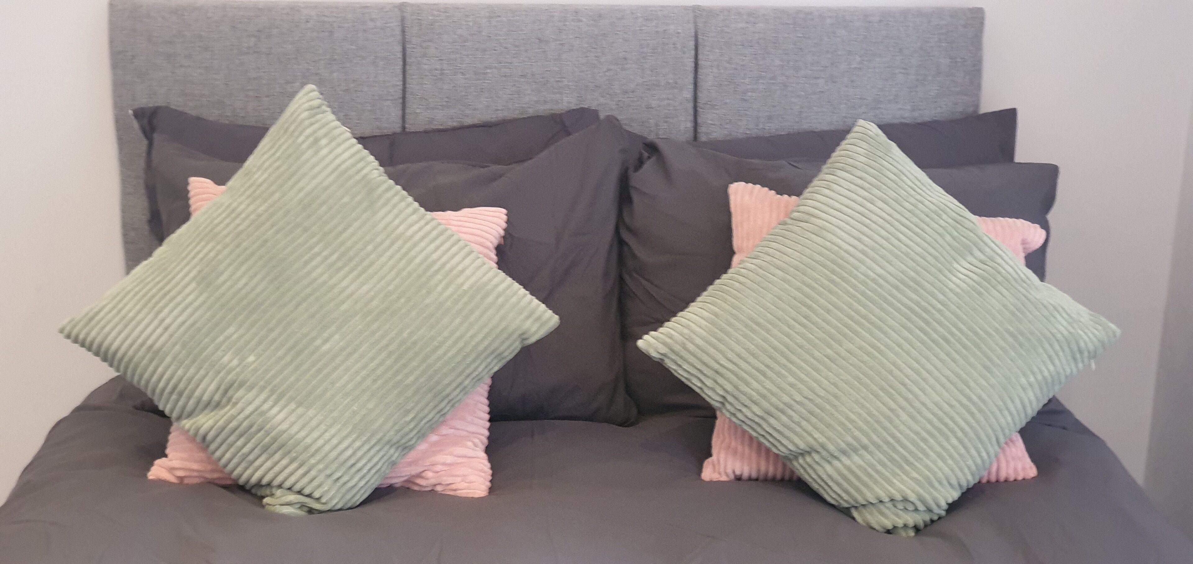 A bed with a grey headboard, multiple pillows in shades of grey and pink, and a grey bedspread.