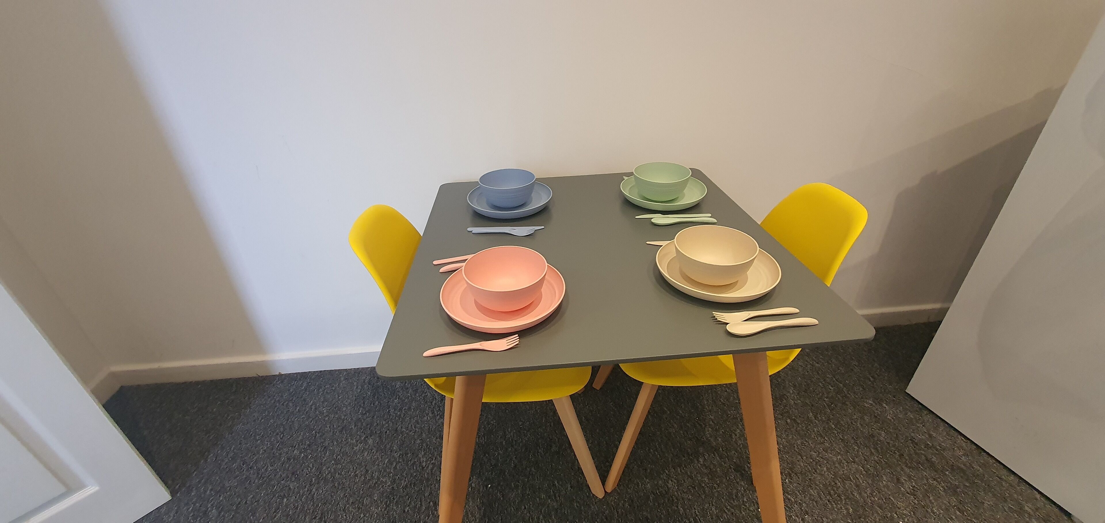 A table set with four bowls and cutlery, surrounded by yellow chairs.