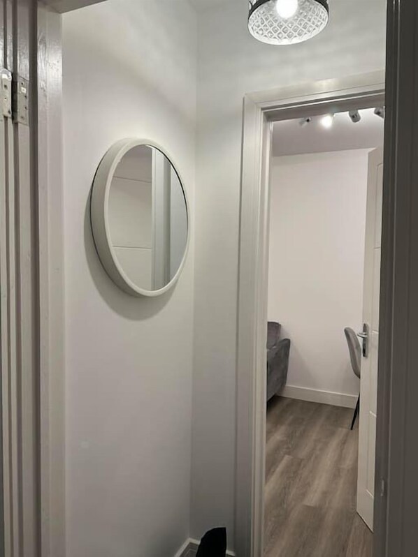 A hallway with a round mirror on the wall, a door leading to another room, and a ceiling light fixture.
