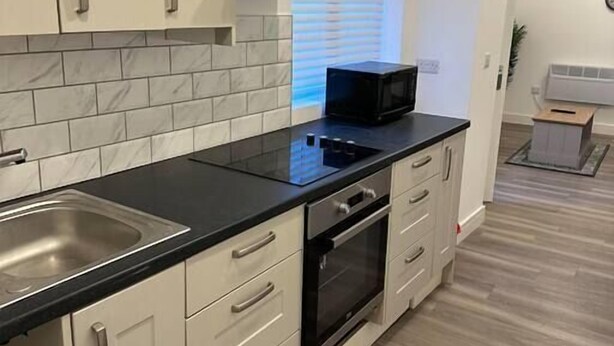 A modern kitchen with white cabinets, a black countertop, a microwave, and a stove. - Flat in Luton Town Centre (Luton)