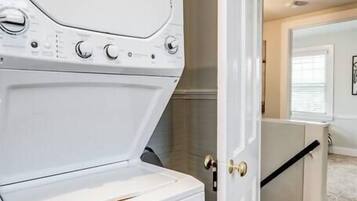 A laundry room with a white washer and dryer, a door leading to another room, and a carpeted floor.