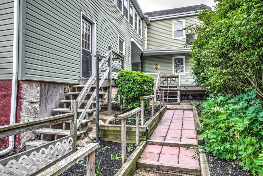 A residential property with a wooden staircase leading to a front door, a small garden area with a wooden fence, and a paved walkway.