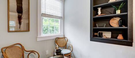 Een kamer met twee rieten stoelen, een bijzettafeltje met een vaas, een boekenkast met diverse voorwerpen, en een lijst met een veer aan de muur.