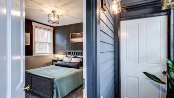 A bedroom with a bed, bedside table, lamp, window, and a door.