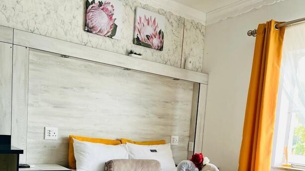 Un dormitorio con una cama, mesitas de noche, una silla y cuadros en la pared.