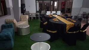 Un salón de conferencias con mesas redondas, sillas negras con detalles dorados y una alfombra verde.