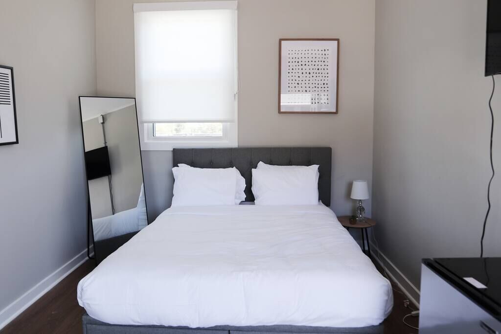 A neatly arranged hotel room with a bed, a bedside table with a lamp, a mirror, and a framed artwork on the wall.