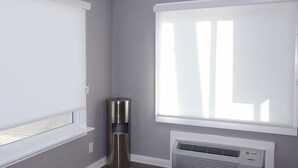 Una habitación con ventana, aire acondicionado de pared y un cubo de basura.