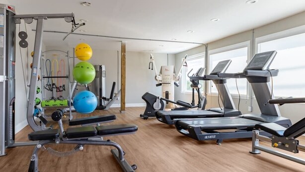 Un gimnasio con cintas de correr, máquinas de pesas y pelotas de ejercicio.
