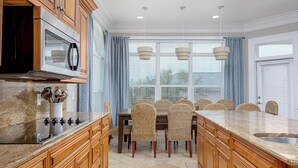 Una cocina con armarios de madera, encimera de granito, microondas integrado y un comedor con sillas de mimbre y una isla grande.
