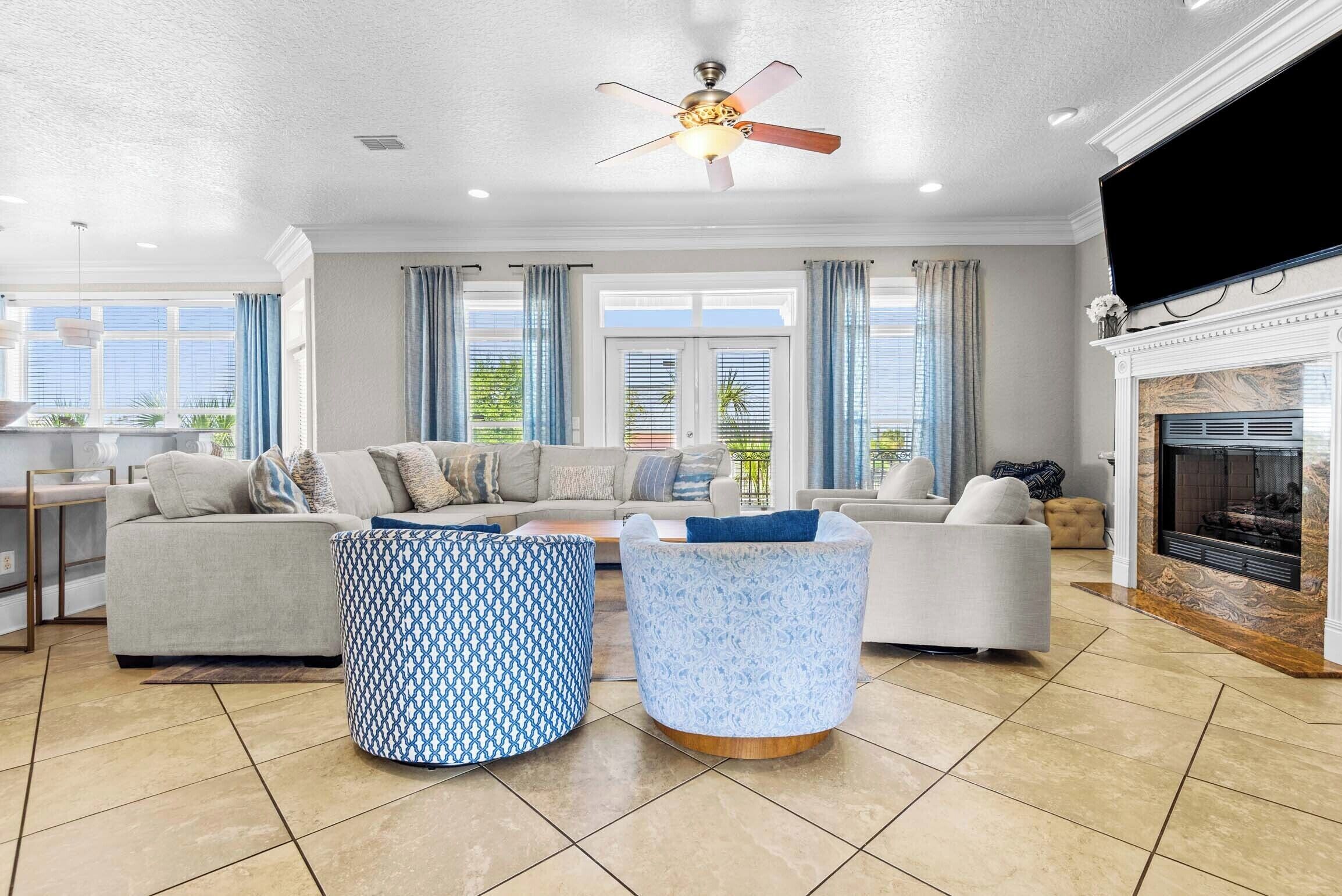 A spacious living room with a fireplace, a ceiling fan, and a large TV.