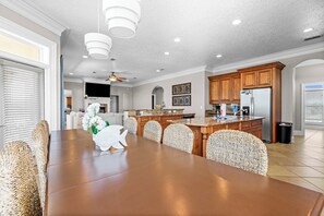 A spacious kitchen with wooden cabinets, a large island, and a dining area with wicker chairs. - 🌊 Palm Palace | Private Pool + Game Room | 6BR Pensacola Beach Retreat (Pensacola Beach)