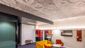 A modern hotel room with a large bed, a sofa, two armchairs, a small table, a TV, and a wardrobe with red and black shelves. - Ibis Baku City Hotel (Baku)