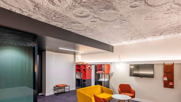 A modern hotel room with a large bed, a sofa, two armchairs, a small table, a TV, and a wardrobe with red and black shelves. - Ibis Baku City Hotel (Baku)