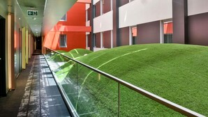 A corridor with a glass railing, green artificial grass, and modern buildings with red and white facades. - Ibis Baku City Hotel (Baku)