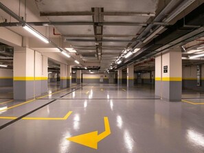 A multi-level parking garage with clear directional arrows on the floor, concrete pillars, and overhead lighting. - Ibis Baku City Hotel (Baku)