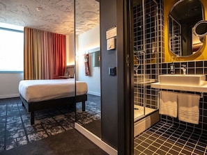 A hotel room with a bed, a shower area, a sink, and a large mirror. - Ibis Baku City Hotel (Baku)