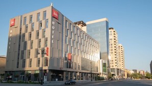 A modern hotel with a prominent 'Ibis' sign, a glass facade, and a corner location. - Ibis Baku City Hotel (Baku)