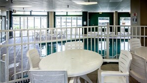A poolside area with a round table and white plastic chairs, surrounded by a white railing.
