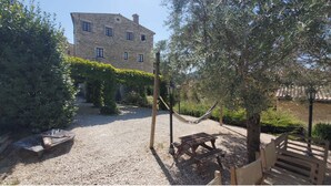 A stone building with a garden featuring a hammock, picnic table, and wooden bench. - Characteristic stone house (Le Poët-Laval)