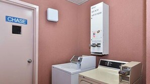 A room with a white door labeled 'CHASE,' a white washing machine, a white dryer, and a white utility cabinet with a thermostat. - Quality Inn Brookhaven, MS (Brookhaven)