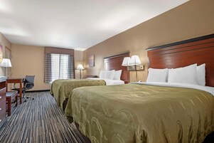 A hotel room with two beds, a desk, and a chair.