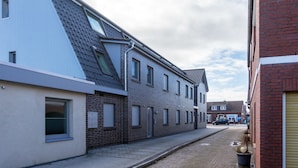 En smal gade med moderne bygninger, herunder en toetages bygning med saddeltag og facade i mursten.
