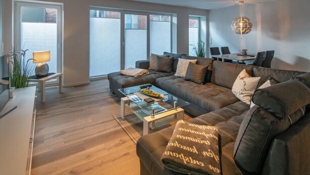 En moderne stue med en lædersofa, et glashøjt sofabord og et spiseområde med bord og stole.