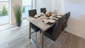 En spiseplads med et bord dækket til fire personer, inklusive tallerkener, glas og en skål med frugt.