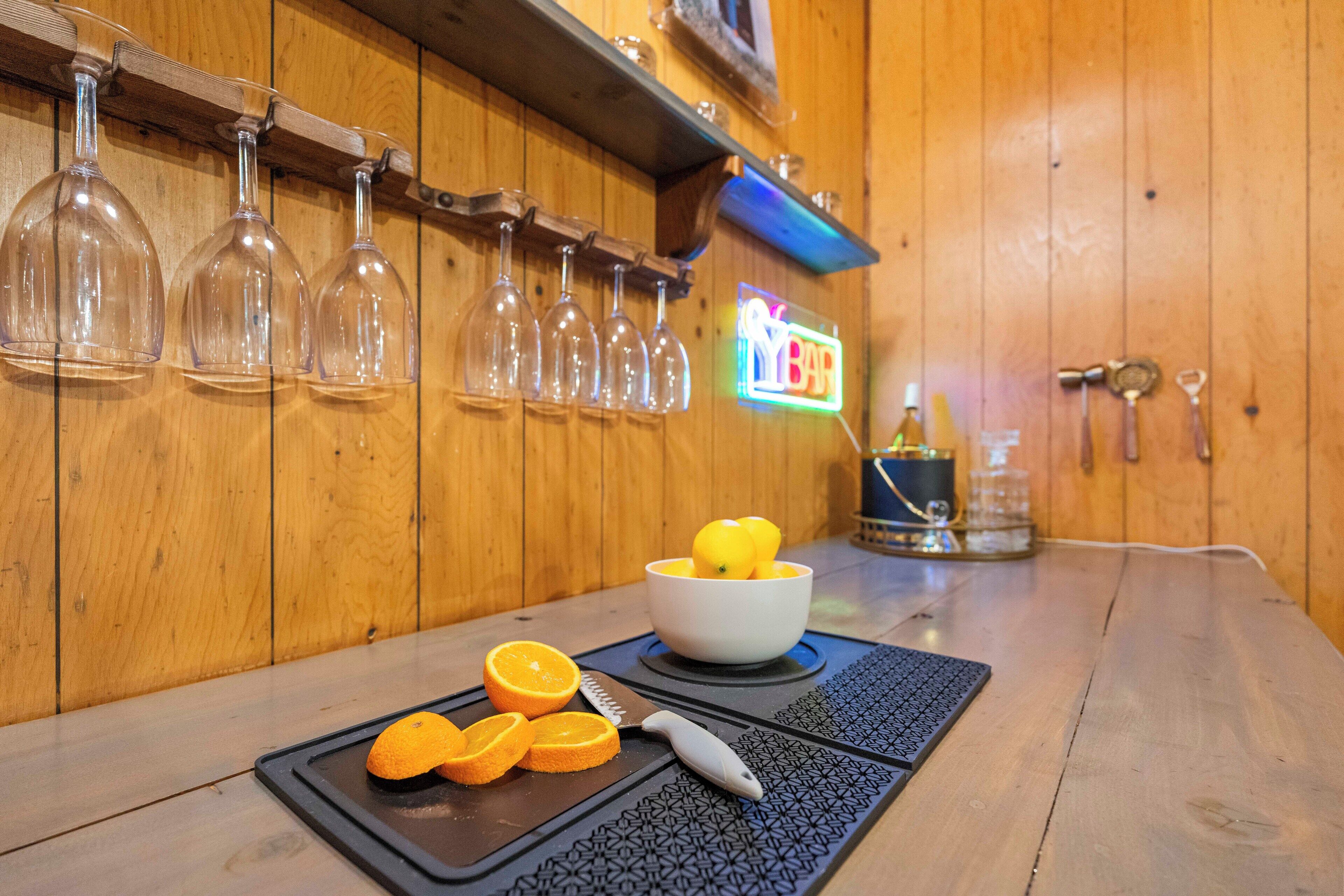 A bar area with wine glasses on a rack, a bowl with lemons, and a cutting board with orange slices.