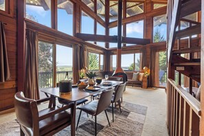 Une salle à manger spacieuse avec un haut plafond et de grandes fenêtres, des meubles en bois et une vue sur l’extérieur.