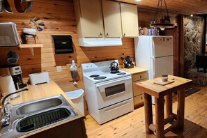 Eine kleine Küche mit Holzwänden, einem weißen Herd, einem Spülbecken und einem Holztisch.
